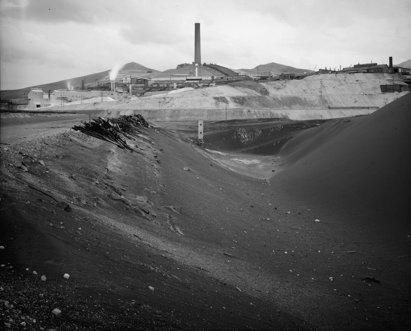 The Big Stack rising over the smelter buildings, a black slag slope in the foreground