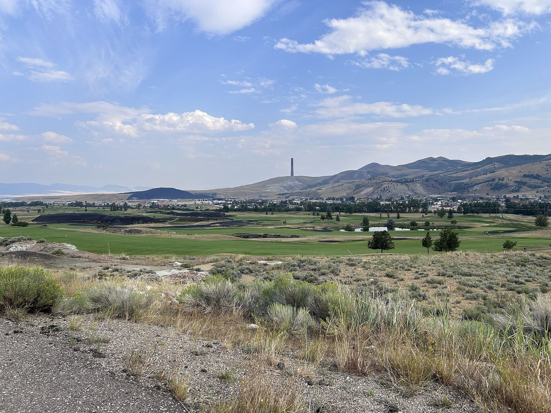 Green fairways of the Old Works golf course in the valley with the stack on the hills beyond, 2024